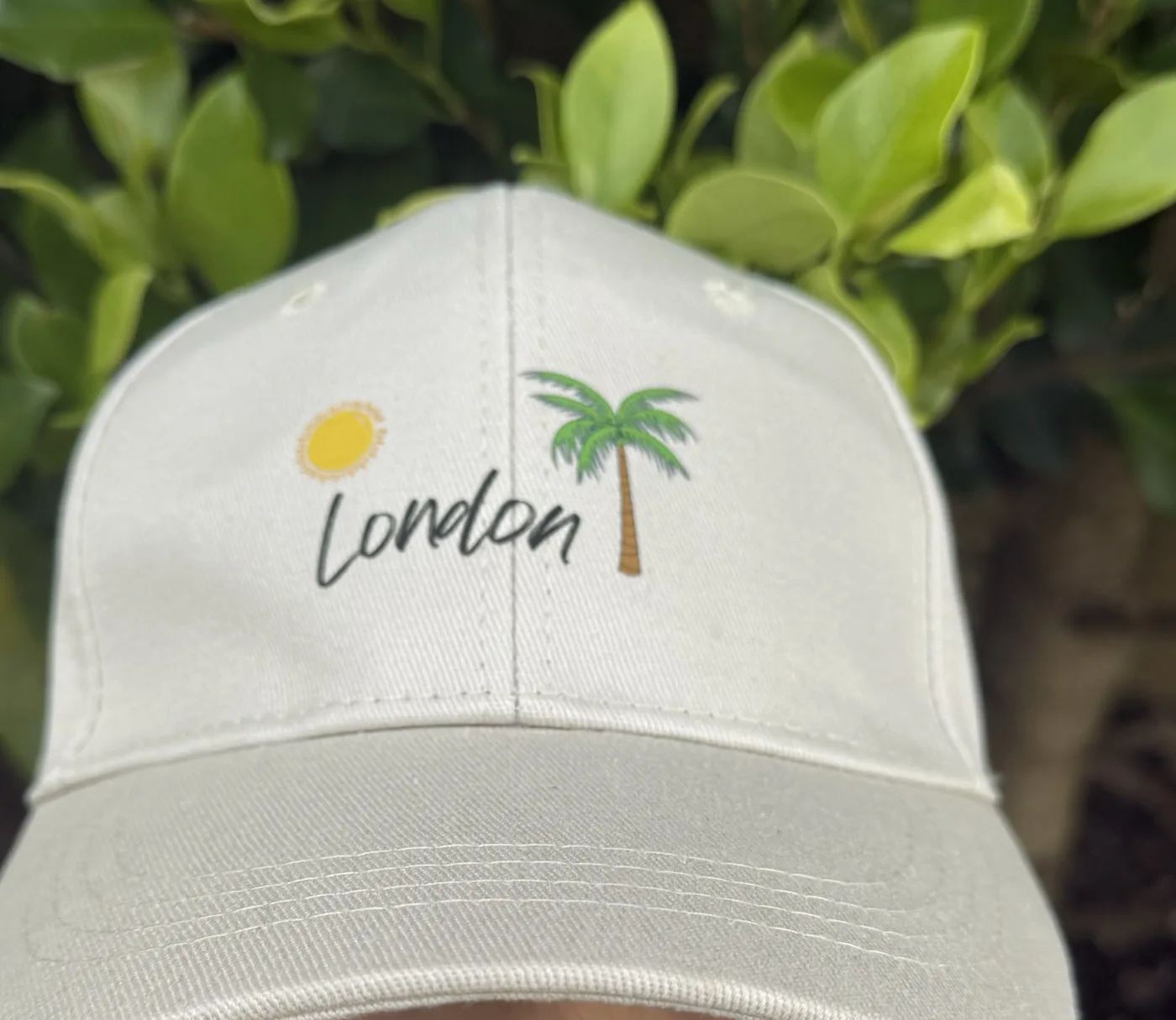 London wearing a tan cap with a sun, the word London and a palm tree, peak pulled down